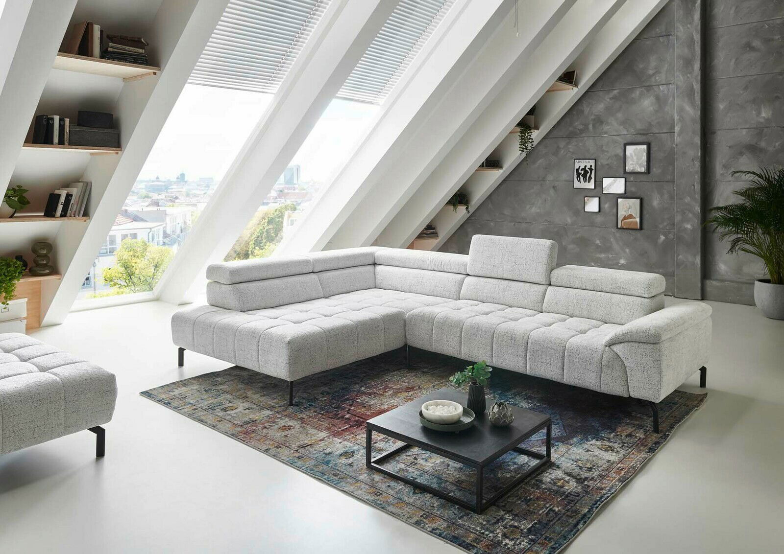 Moderne Eckgarnitur in hellem Stoffbezug, präsentiert in einem stilvollen Wohnzimmer mit schrägen Fenstern und urbanem Ausblick, aus seitlicher Perspektive fotografiert.