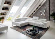 Moderne Eckgarnitur in hellem Stoffbezug, präsentiert in einem stilvollen Wohnzimmer mit schrägen Fenstern und urbanem Ausblick, aus seitlicher Perspektive fotografiert.