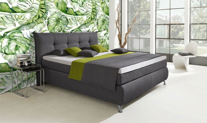 Boxspringbett in modernem Design mit grauem Stoffbezug, grünen Akzenten und mehreren Kissen, seitliche Perspektive