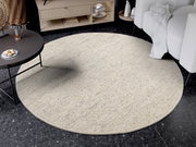 Runder, handgewebter Teppich in hellem Beige auf dunklem Marmorboden, umgeben von einem modernen Couchtisch und einem weißen Sofa. Perspektive von oben.