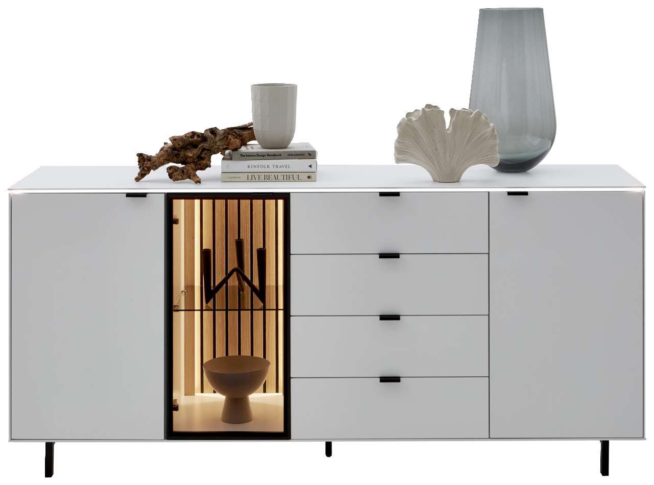 Modernes weißes Sideboard mit vier Schubladen und zwei Türen, eine davon mit Glas und Beleuchtung. Dekoriert mit Büchern, einer Tasse, einer Vase und einer Skulptur. Frontale Perspektive.