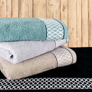 Ein Stapel von Handtüchern in verschiedenen Farben, darunter Türkis, Grau und Beige, mit dekorativen Mustern, auf einem Holzhintergrund. Perspektive von der Seite.