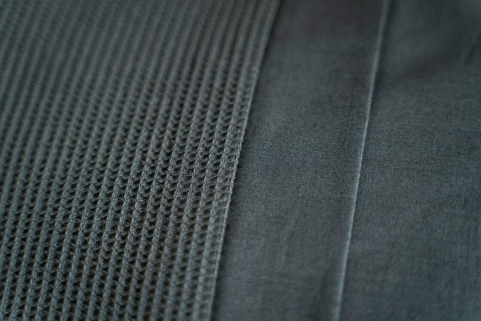 Nahaufnahme einer Bettwäsche mit strukturierter und glatter Oberfläche in dunklem Grau.