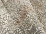 Nahaufnahme eines Designer-Teppichs mit abstraktem Muster in Grau- und Beigetönen, perspektivisch von der Seite aufgenommen.