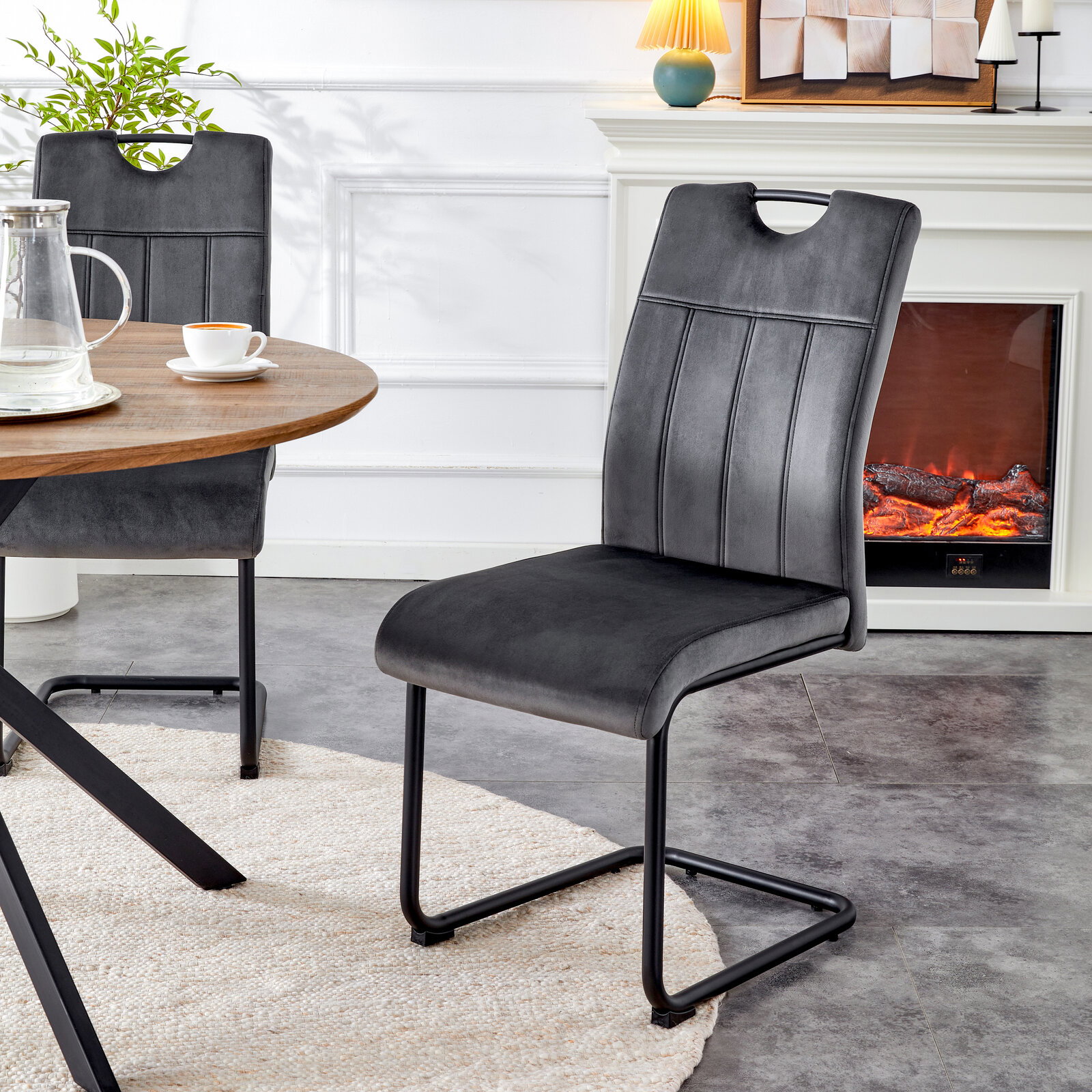 Dunkelgrauer Polster-Esszimmerstuhl in Veloursoptik mit Steppnähten, Griffausschnitt und schwarzem Metall-Kufengestell, in schräger Vorderansicht am Esstisch im Wohnraum