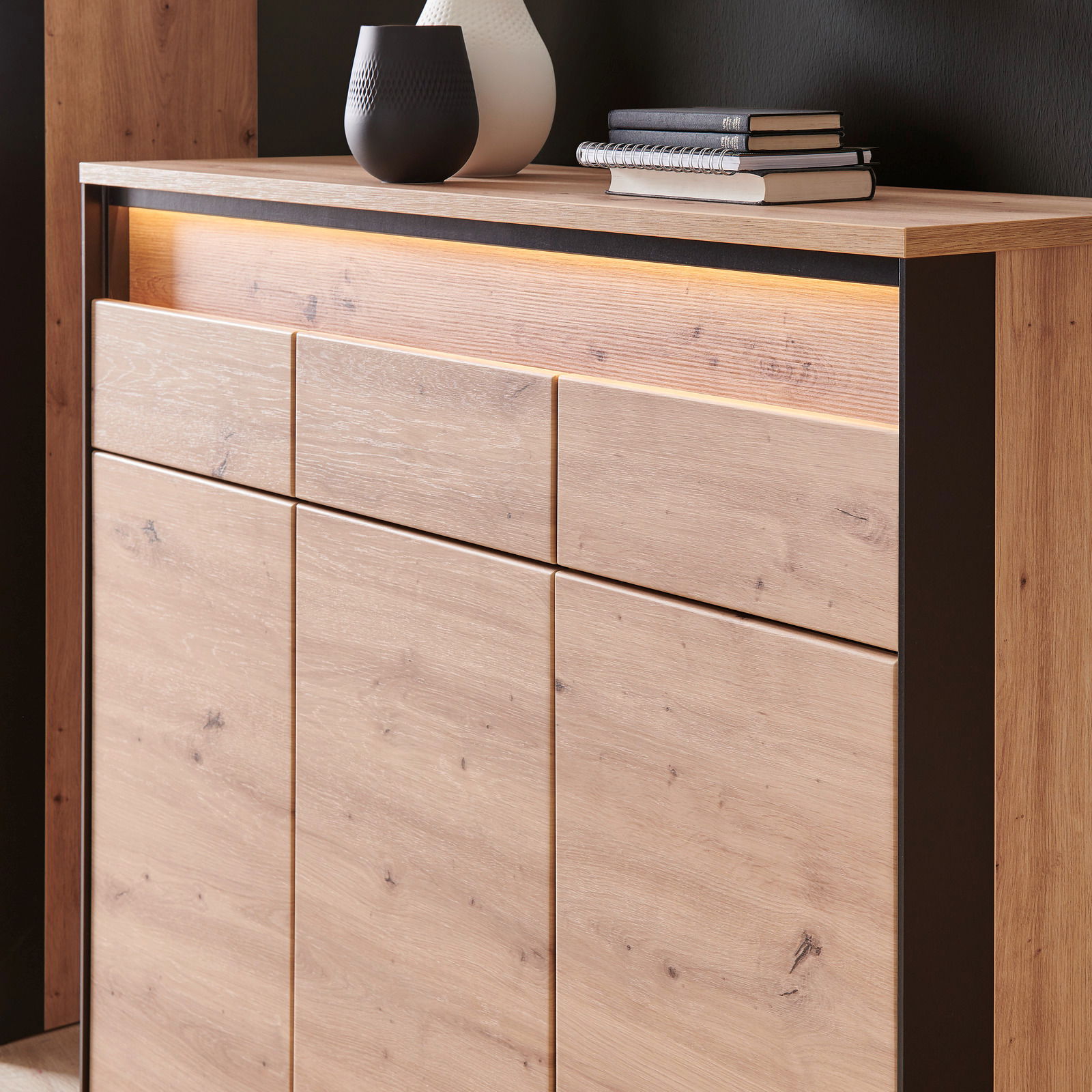 Nahaufnahme eines XL-Schuhschranks aus Holz mit moderner LED-Beleuchtung, dekoriert mit Vasen und Büchern auf der Oberseite, seitliche Perspektive.