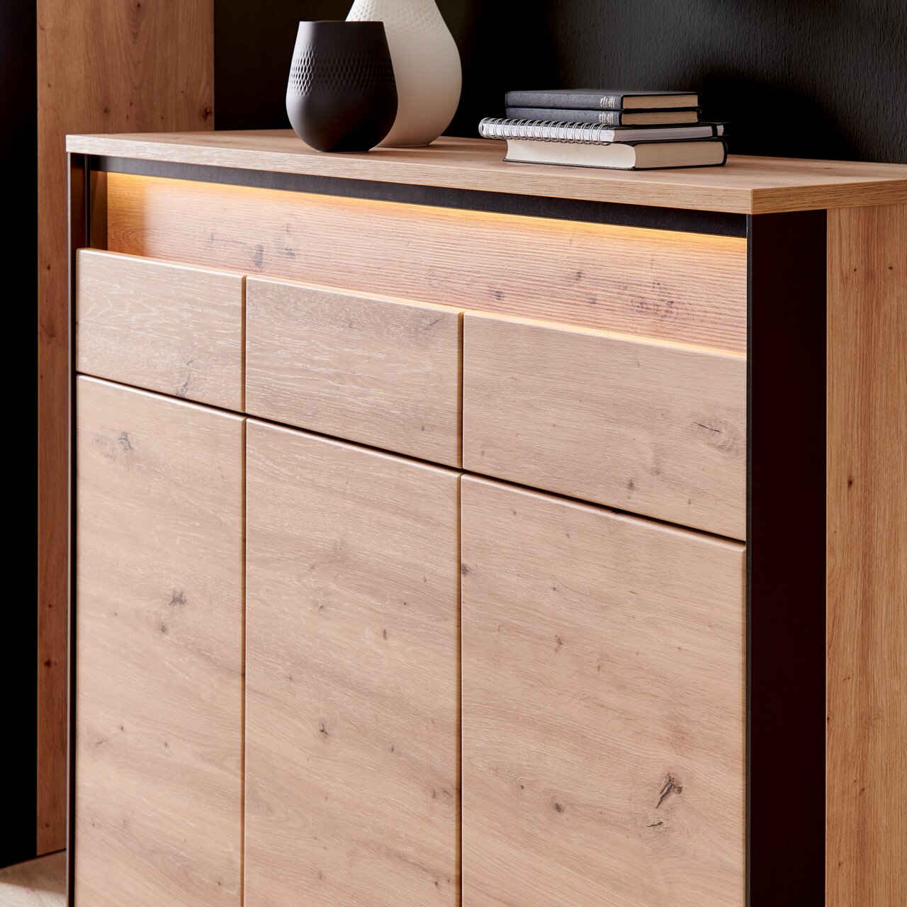 Close-up van een grote houten schoenenkast met moderne ledverlichting, versierd met vazen en boeken op het bovenste blad, gezien vanuit de zijkant.