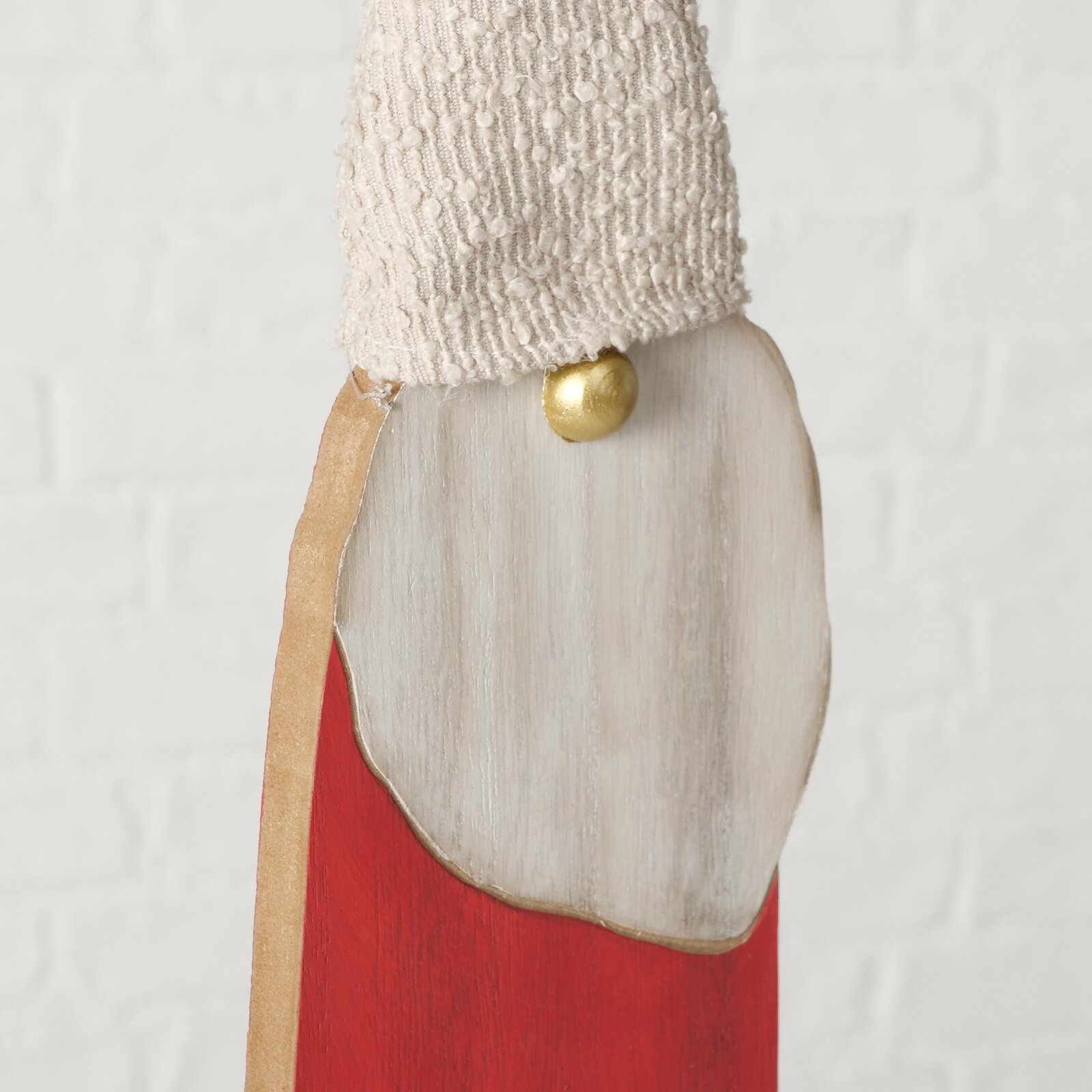 Nahaufnahme einer dekorativen Figur mit rotem Körper, weißem Bart und gestrickter Mütze, seitliche Perspektive.