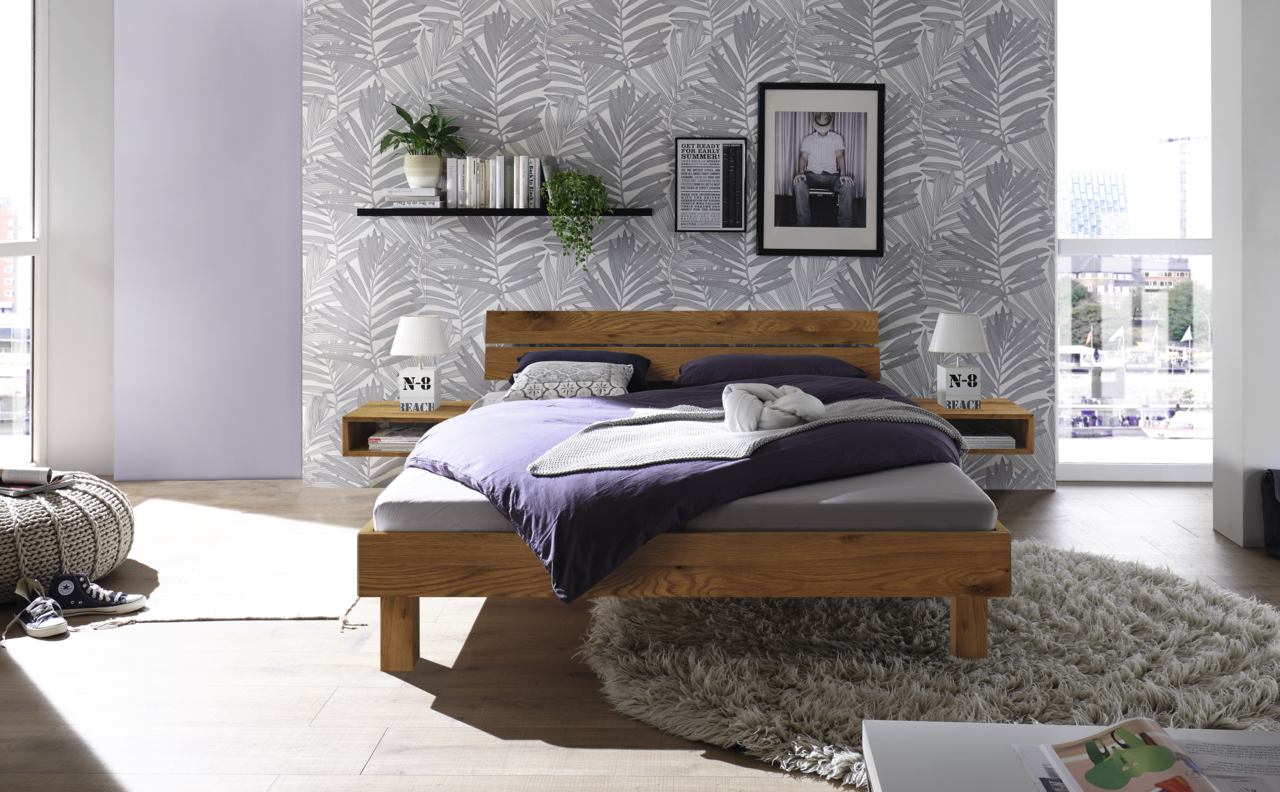 Modernes Schlafzimmer mit einem Kopfteil aus Holz und Metall, frontal betrachtet. Das Bett ist mit lila Bettwäsche bezogen und von stilvollen Nachttischen flankiert. Im Hintergrund eine dekorative Tapete mit Pflanzenmuster.