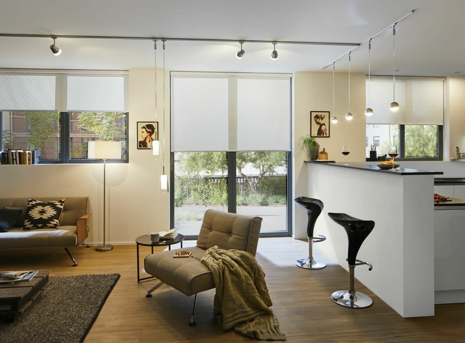 Moderne Wohnzimmeransicht mit stilvollen LED-Leuchten an der Decke und über der Theke, gemütliche Sitzecke mit Sofa und Sessel, Tageslicht durch große Fenster.