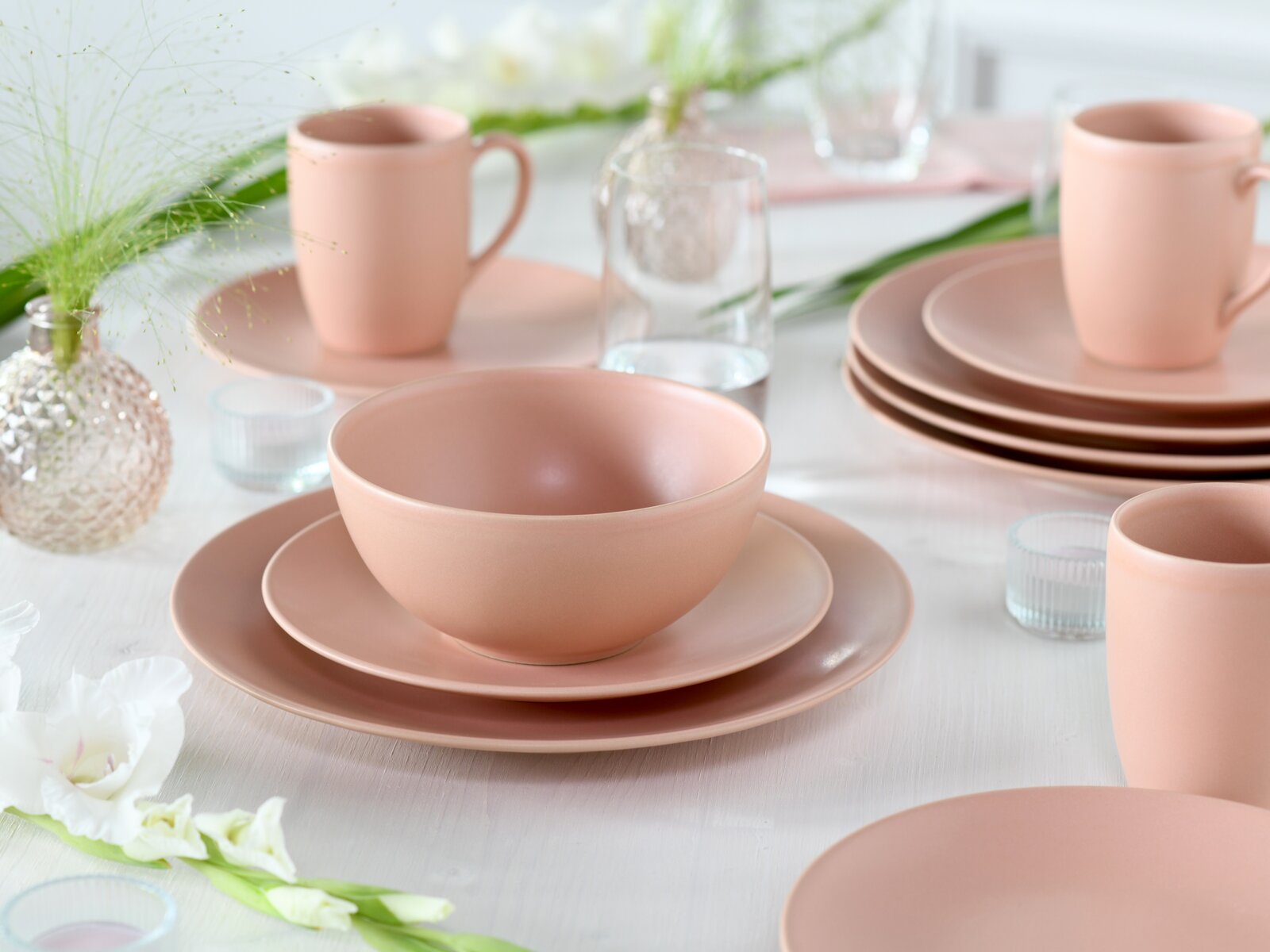 Pastellrosa Geschirr-Set mit Schüssel auf Teller und Tassen auf gedecktem Tisch, fotografiert aus leicht erhöhter, schräger Frontperspektive