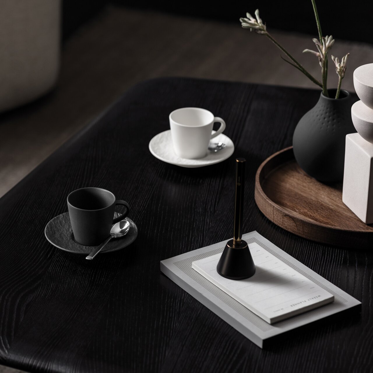 Zwei Espressotassen auf einem dunklen Holztisch, eine in Schwarz und eine in Weiß, mit passenden Untertassen und Löffeln, aus einer seitlichen Perspektive fotografiert.