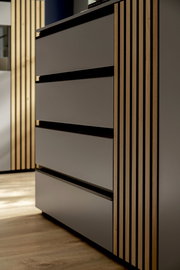 Nahaufnahme eines modernen Sideboards mit glatten, grauen Fronten und vertikalen Holzstreifen an der Seite, aus seitlicher Perspektive fotografiert.