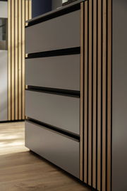 Nahaufnahme eines modernen Sideboards mit glatten, grauen Fronten und vertikalen Holzstreifen an der Seite, aus seitlicher Perspektive fotografiert.