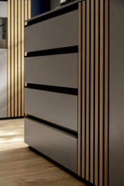 Nahaufnahme eines modernen Sideboards mit glatten, grauen Fronten und vertikalen Holzstreifen an der Seite, aus seitlicher Perspektive fotografiert.