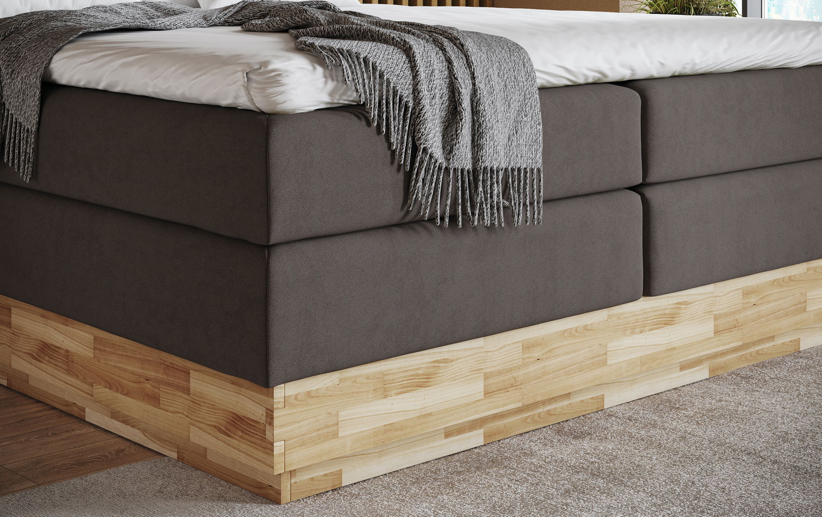 Nahaufnahme eines Boxspringbetts mit grauem Stoffbezug und Holzunterbau, seitliche Perspektive