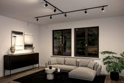 Moderne Wohnzimmeransicht mit Schienenspot Luxe Beleuchtung an der Decke, grauem Sofa, schwarzem Sideboard und großen Fenstern mit Blick auf den Garten.