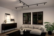 Moderne Wohnzimmeransicht mit Schienenspot Luxe Beleuchtung an der Decke, grauem Sofa, schwarzem Sideboard und großen Fenstern mit Blick auf den Garten.