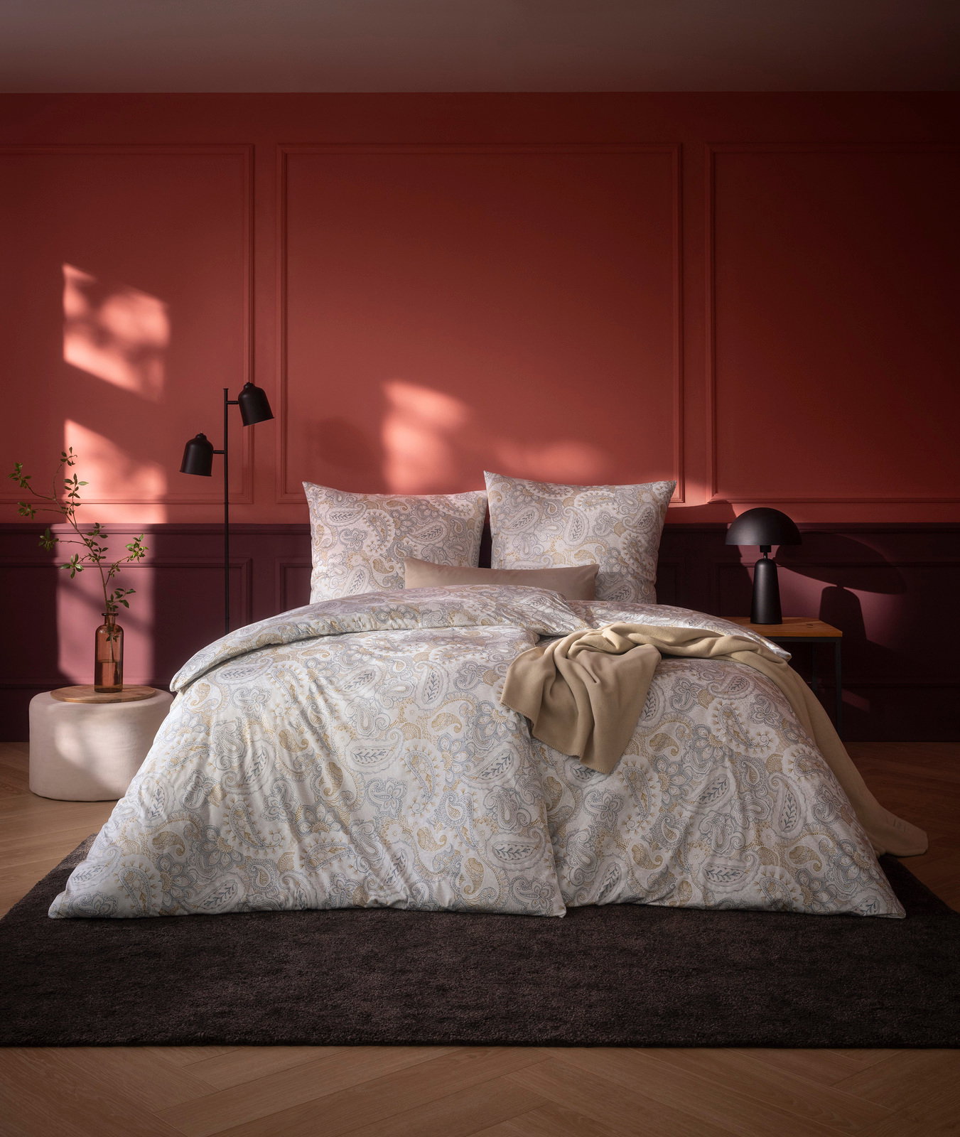 Bettwäsche-Set in einem stilvollen Schlafzimmer mit roter Wand, bestehend aus einem Bettbezug und Kissenbezügen mit Paisley-Muster, aus der Perspektive von vorne aufgenommen.