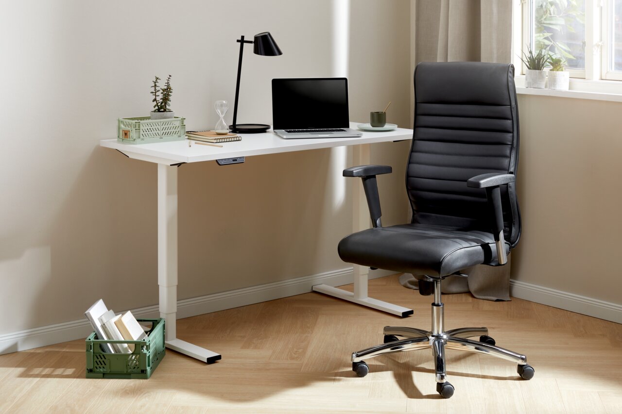 Topstar Chefsessel PROFI CHIEF 100 Moderner Chefsessel in schwarzem Leder, seitliche Perspektive, neben einem weißen Schreibtisch mit Laptop und Lampe.