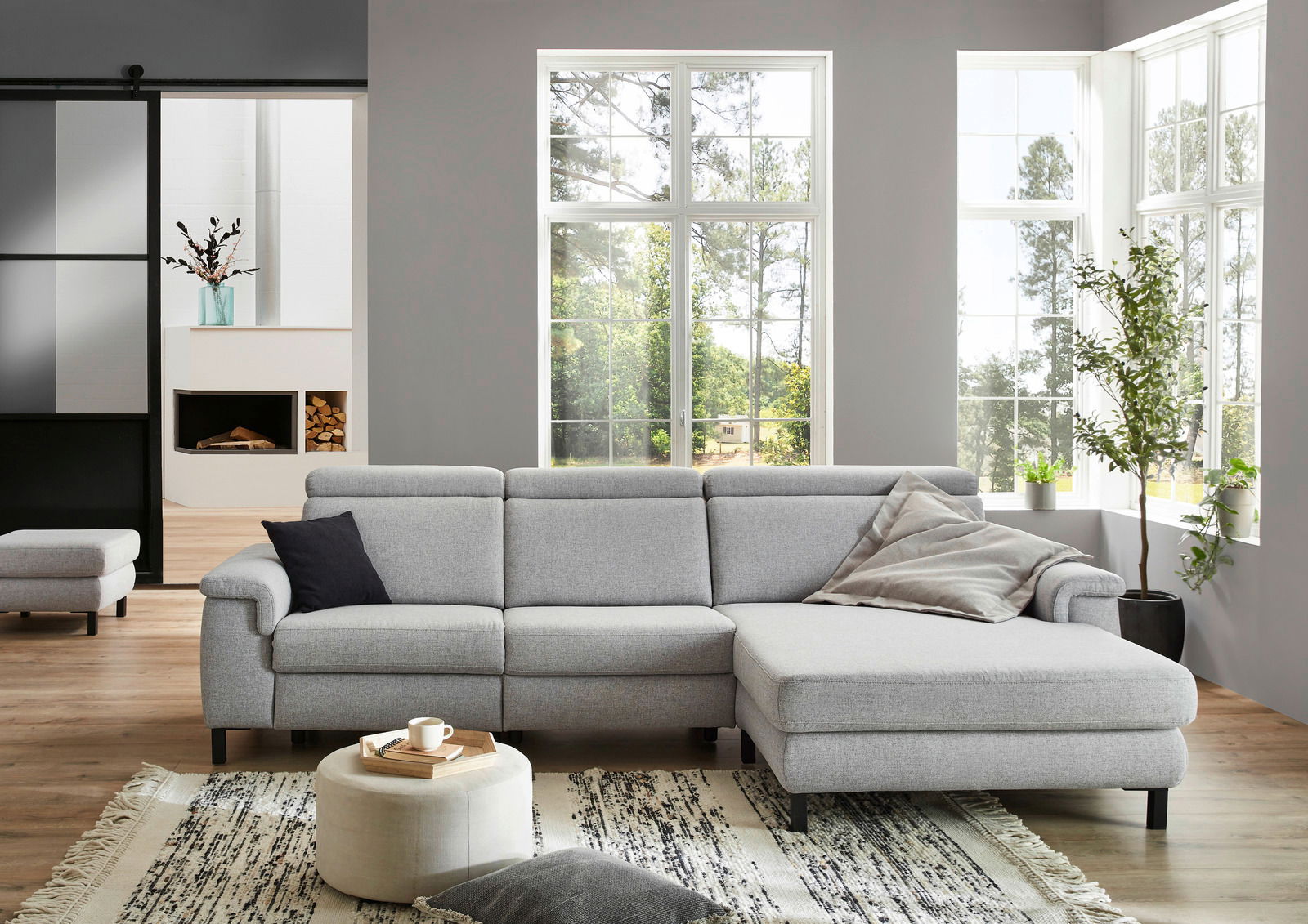 Graue Longchairkombination in einem modernen Wohnzimmer mit großen Fenstern und Holzboden, seitliche Perspektive.