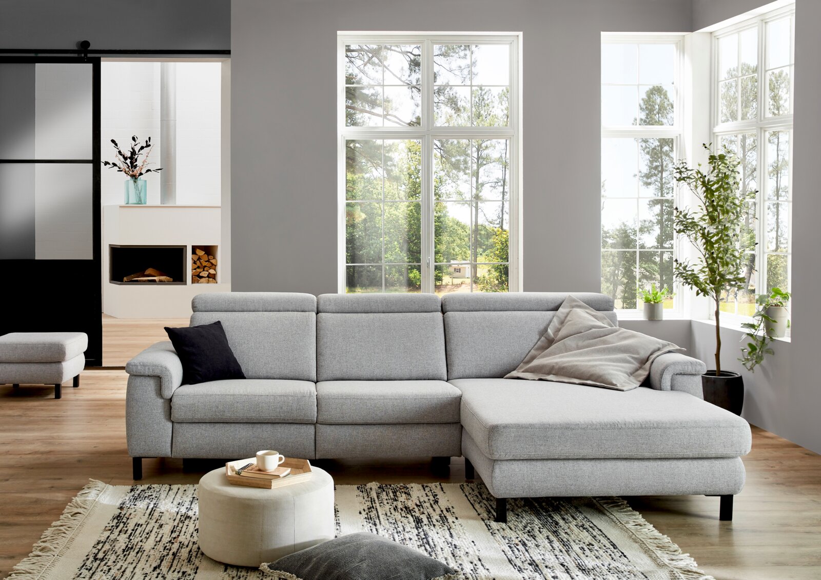 Grijze longchair-set in een moderne woonkamer met grote ramen en een houten vloer, gezien vanaf de zijkant.