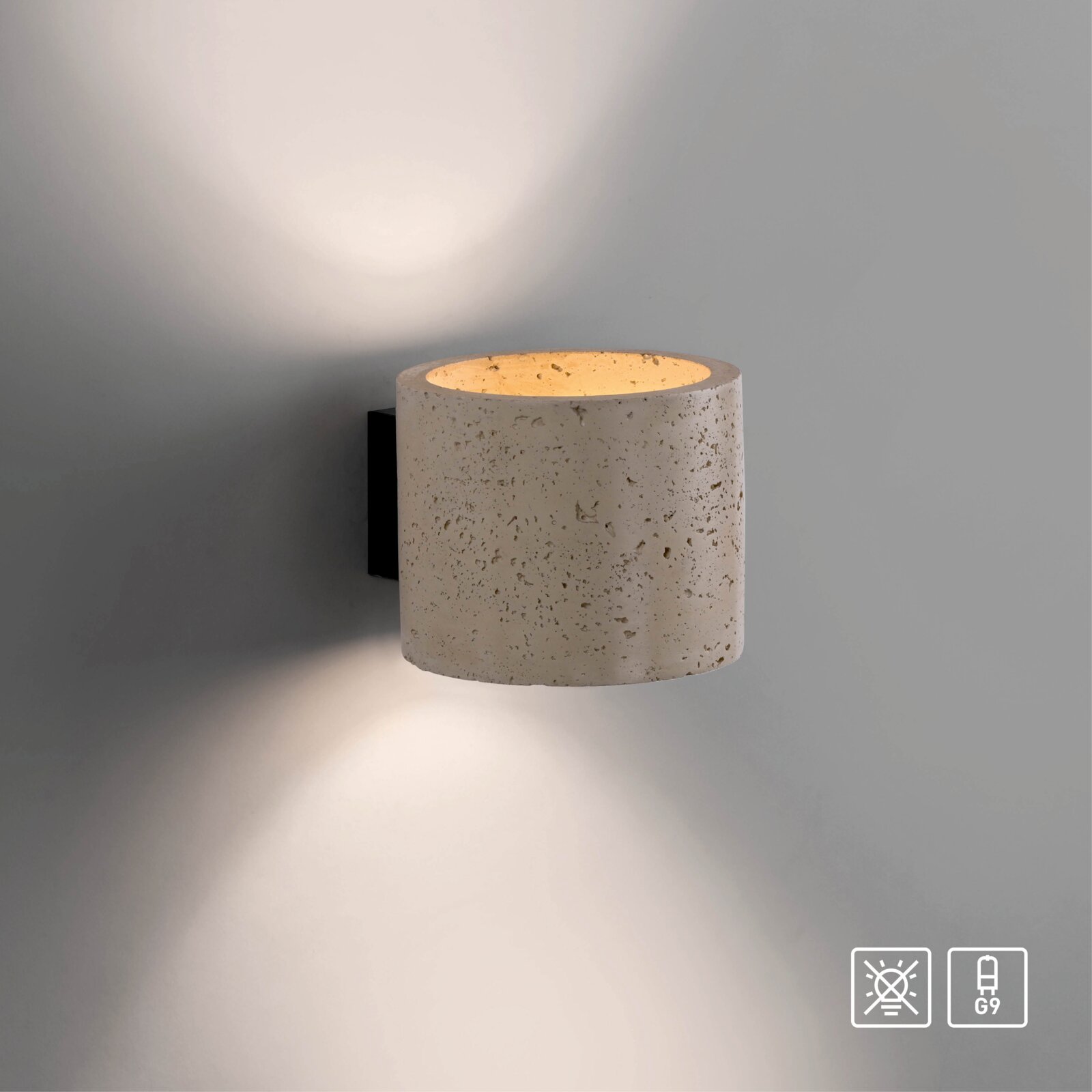 Moderne Wandlampe mit zylindrischem Schirm in Betonoptik und schwarzer Wandhalterung, warmes Licht nach oben und unten an grauer Wand, Frontansicht leicht von rechts.