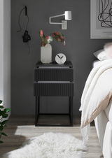 Moderne schwarze Nachtkommode mit zwei Schubladen, dekoriert mit einer Vase und einer Uhr, seitliche Perspektive.