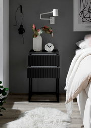 Moderne schwarze Nachtkommode mit zwei Schubladen, dekoriert mit einer Vase und einer Uhr, seitliche Perspektive.