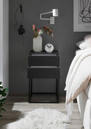 Moderne schwarze Nachtkommode mit zwei Schubladen, dekoriert mit einer Vase und einer Uhr, seitliche Perspektive.