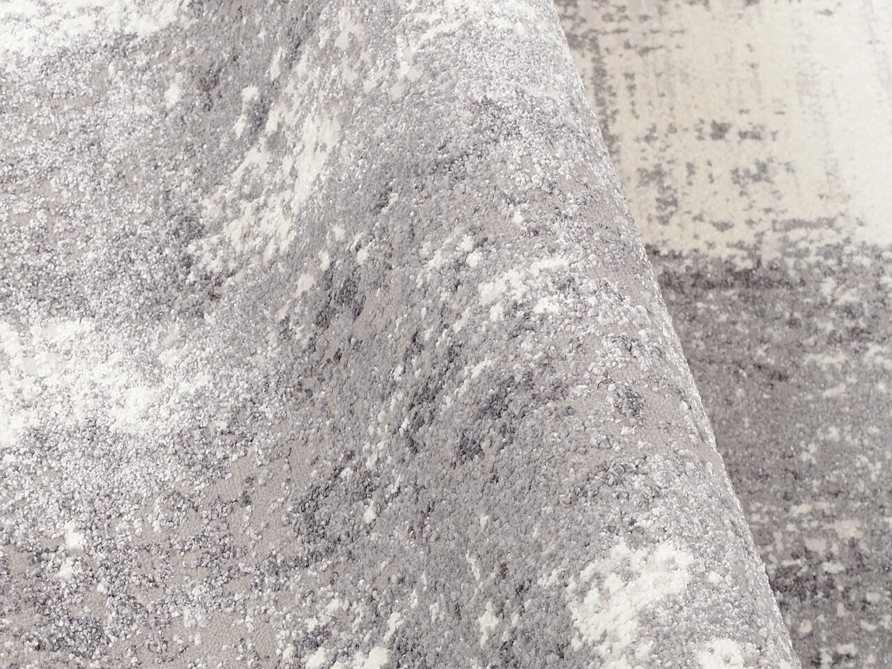 Nahaufnahme eines Designer Teppichs in Grau- und Weißtönen, mit einer leicht gewellten Struktur.