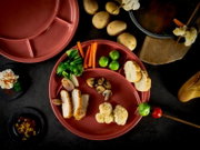 Terrakottafarbener, unterteilter Teller mit verschiedenen Speisen (Hähnchenschnitzelstreifen, Rosenkohl, Karottensticks, Pilze, Blumenkohl, Brot) auf dunklem Untergrund, Draufsicht/Top-Down-Perspektive.