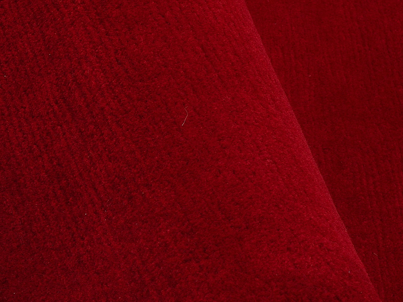 Nahaufnahme eines roten Wollteppichs mit sichtbarer Textur und Falten.