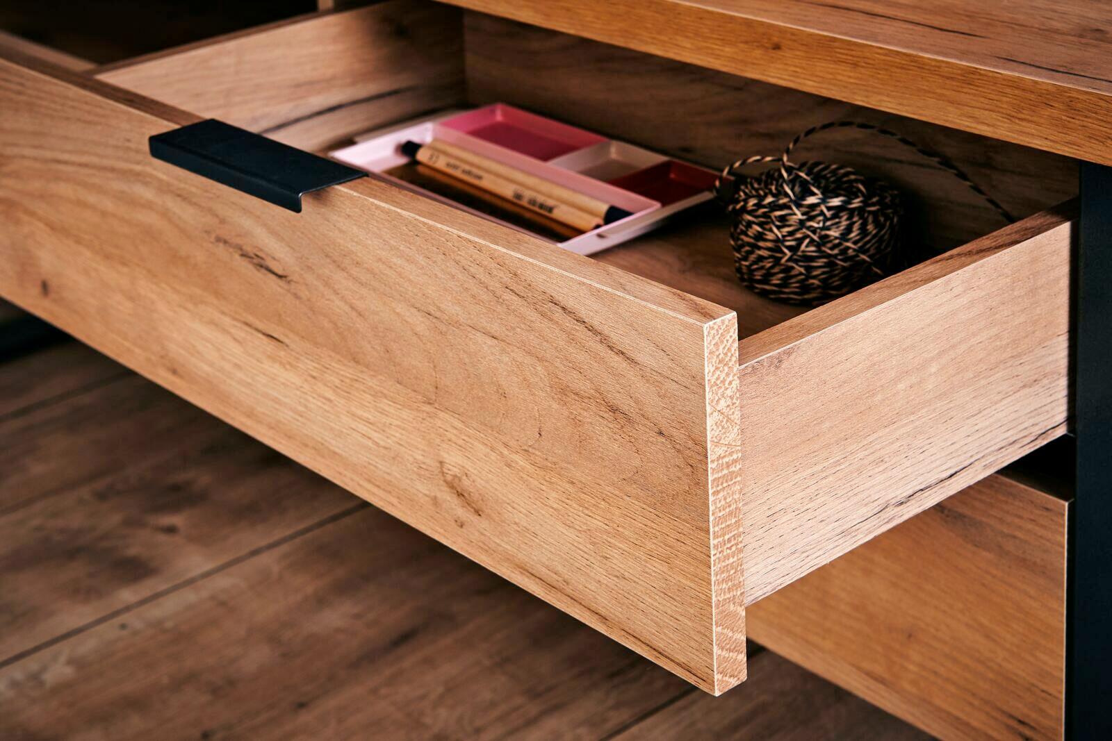 Nahaufnahme einer geöffneten Schublade aus Holz mit schwarzem Griff, gefüllt mit kleinen Gegenständen, von der Seite betrachtet.