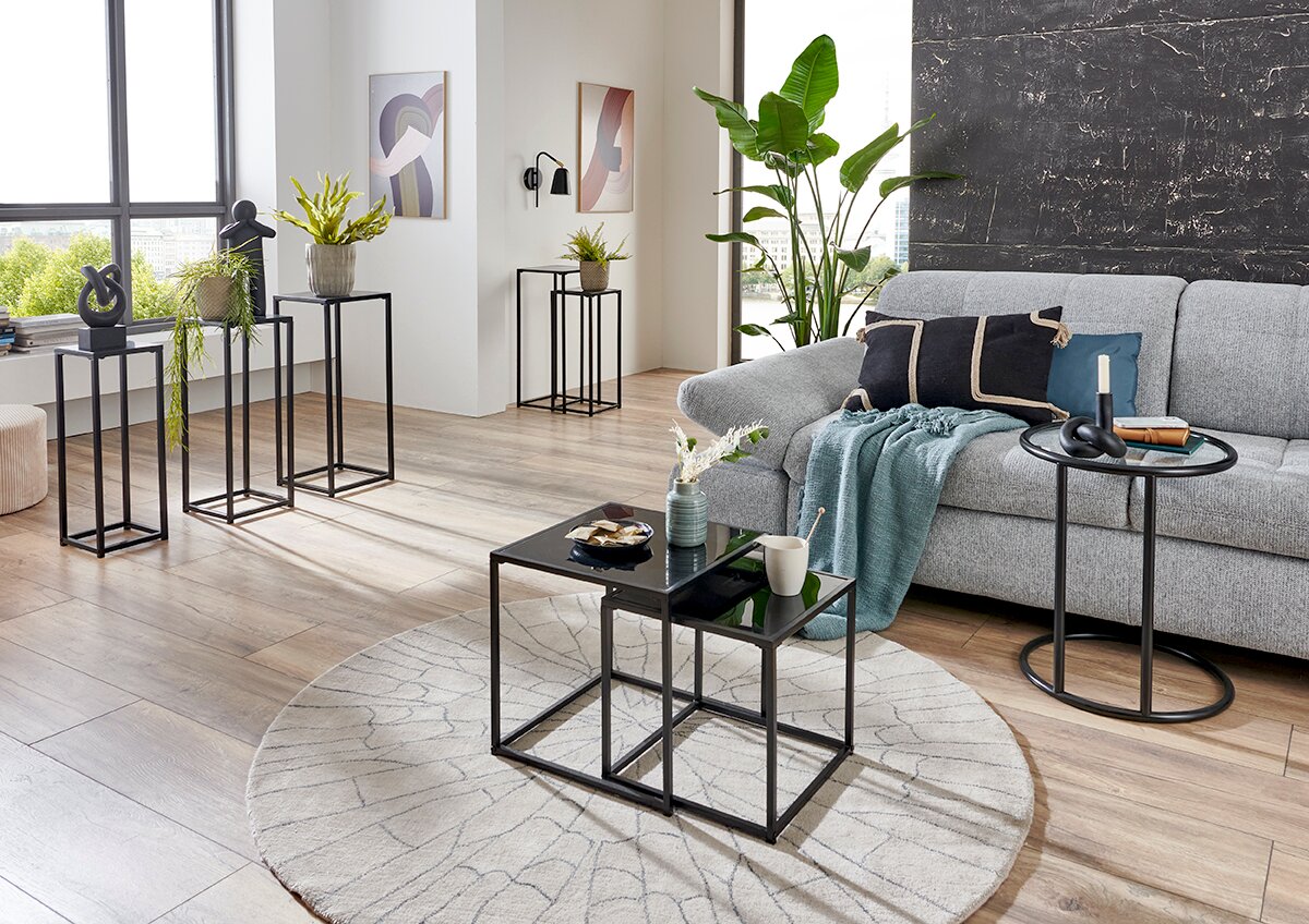 Modernes Wohnzimmer mit grauem Sofa, rundem Beistelltisch und schwarzem, zweiteiligem Couchtisch-Set auf rundem Teppich, fotografiert aus leicht erhöhter Front-Links-Perspektive.