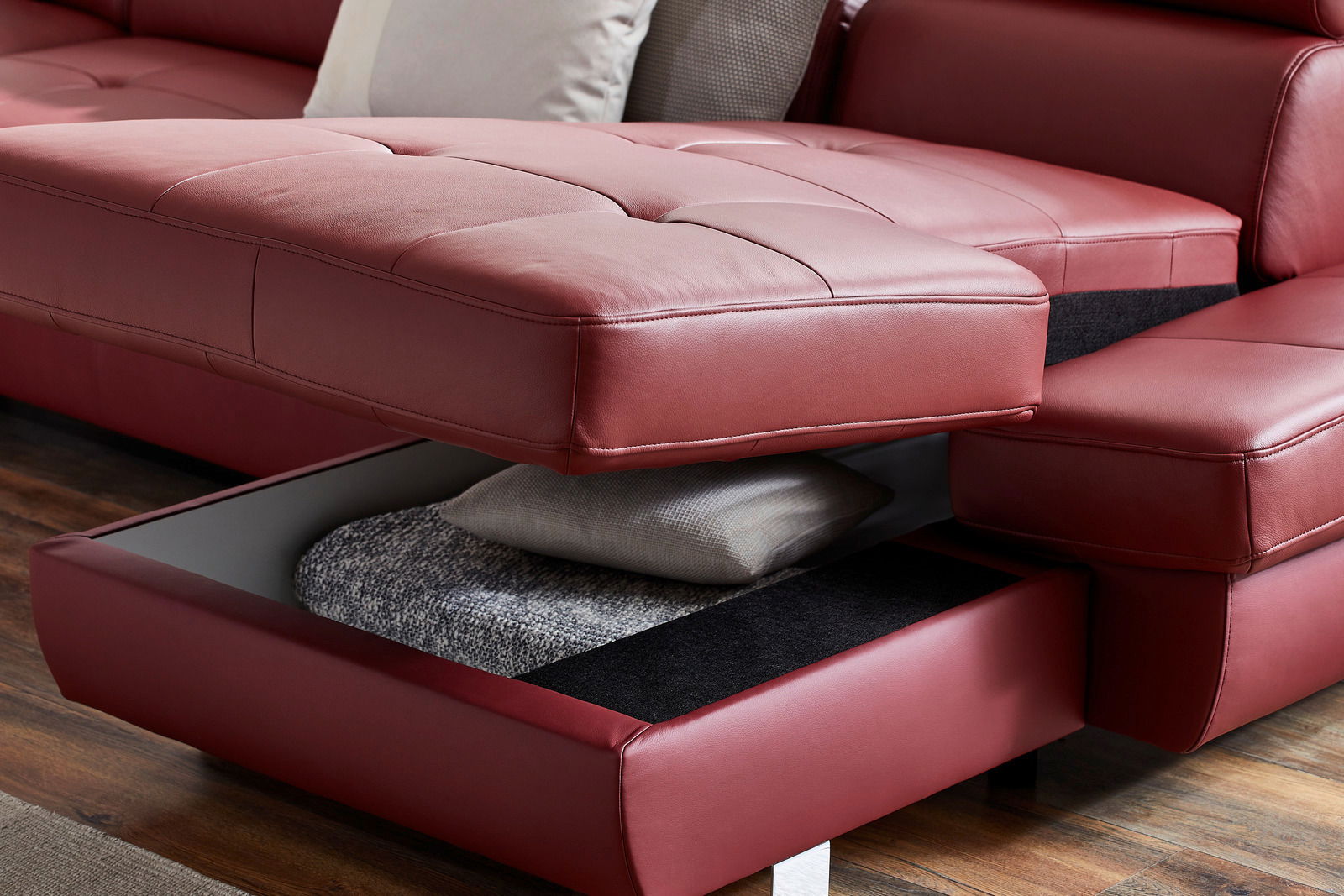 Nahaufnahme einer roten Polsterrundecke TORINO mit Bettfunktion, die einen geöffneten Stauraum mit Kissen und Decke zeigt, aus seitlicher Perspektive.