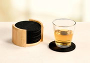 Ein Set aus schwarzen Filzuntersetzern in einem Holzhalter, mit einem Glas auf einem Untersetzer. Perspektive: seitlich.