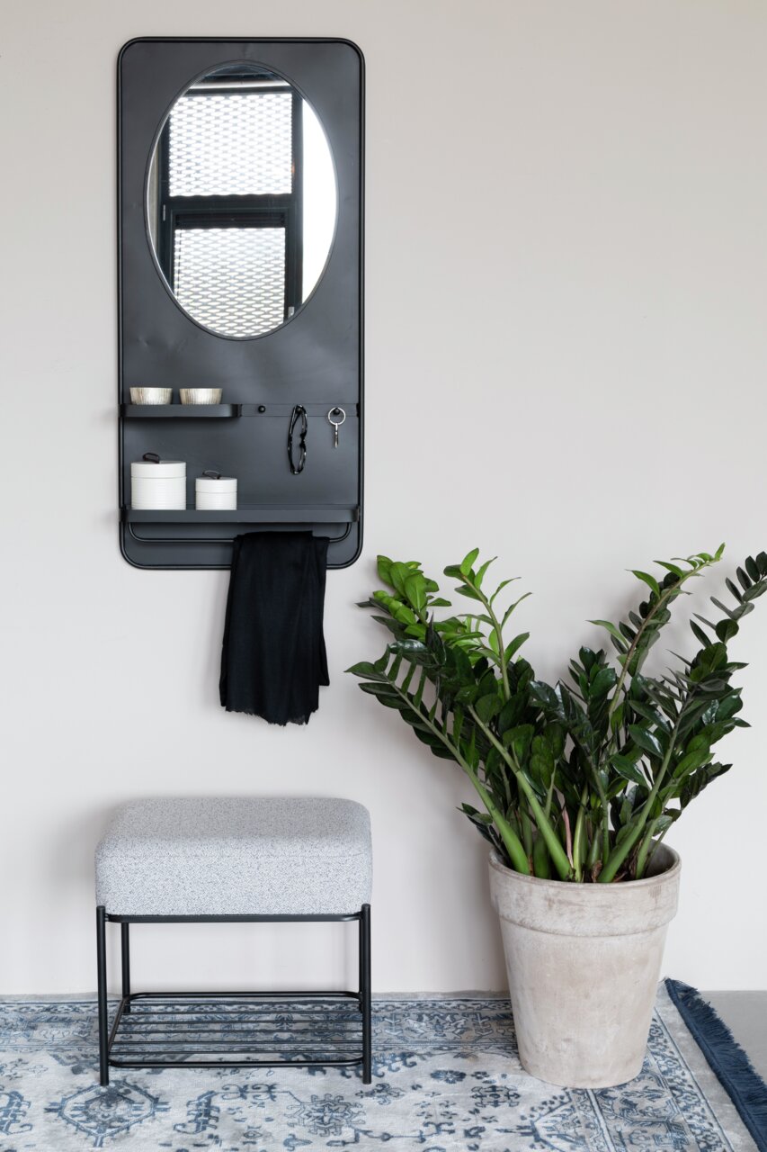 Z2 Kruk MILOU Moderne poef met grijze bekleding en een zwart metalen onderstel, gefotografeerd van voren, naast een grote groene plantenbak op een tapijt met patroon.