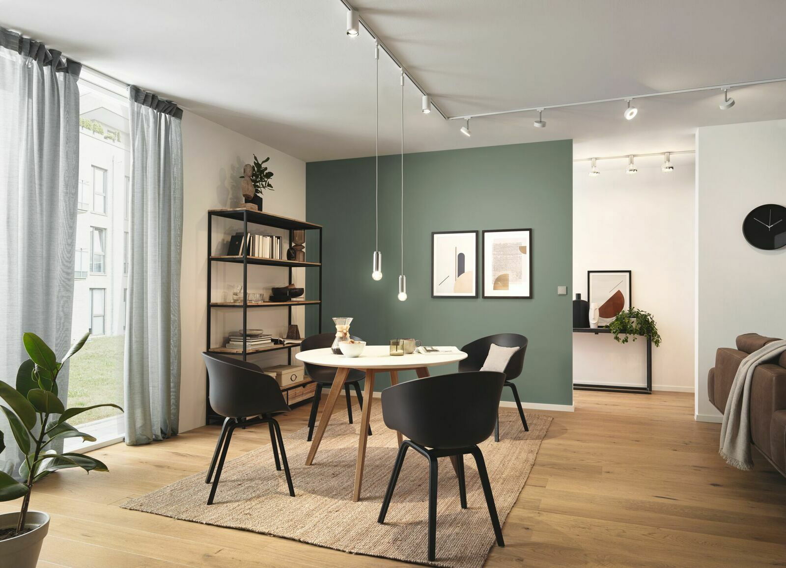 Moderne Wohnzimmerszene mit Schienensystem an der Decke, das mehrere verstellbare Leuchten trägt. Perspektive von der Seite, die den Raum mit Tisch, Stühlen und Regal zeigt.