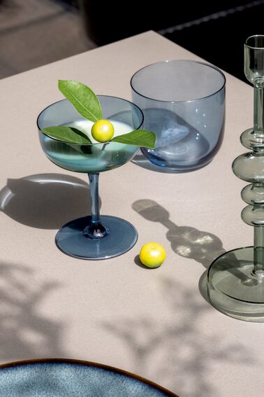 Elegante Sektschale aus blauem Glas mit dekorativer Zitrone und Blättern, von oben fotografiert.