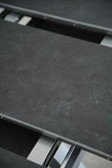 Nahaufnahme eines Esstisches mit dunkler, marmorierter Oberfläche und Metallrahmen, von oben betrachtet.