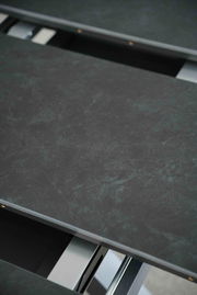 Nahaufnahme eines Esstisches mit dunkler, marmorierter Oberfläche und Metallrahmen, von oben betrachtet.