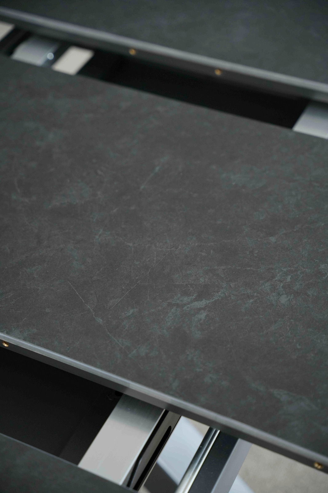 Nahaufnahme eines Esstisches mit dunkler, marmorierter Oberfläche und Metallrahmen, von oben betrachtet.