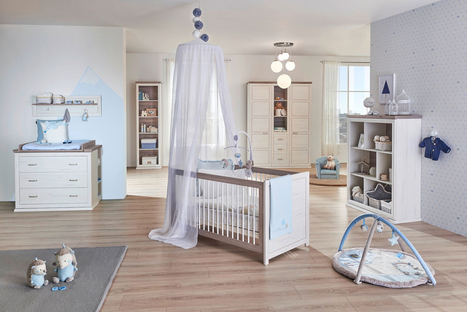 Kinderzimmer mit einem weißen Kinderbett mit Himmel, Wickelkommode und Spielmatte, seitliche Perspektive