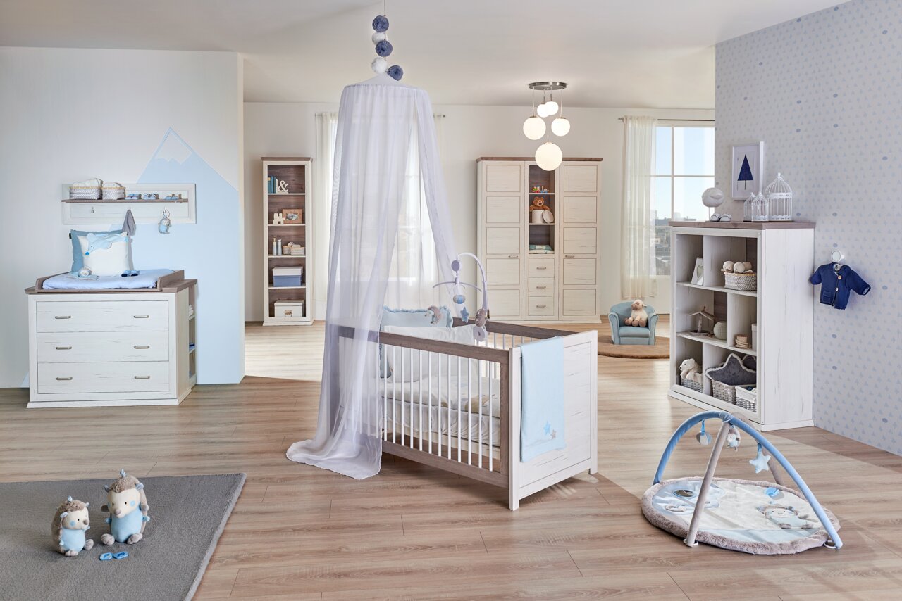 Kinderzimmer mit einem weißen Kinderbett mit Himmel, Wickelkommode und Spielmatte, seitliche Perspektive