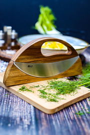 Doppel-Wiegemesser WAVE aus Holz und Edelstahl, seitliche Perspektive, auf einem Schneidebrett mit frischen Kräutern.