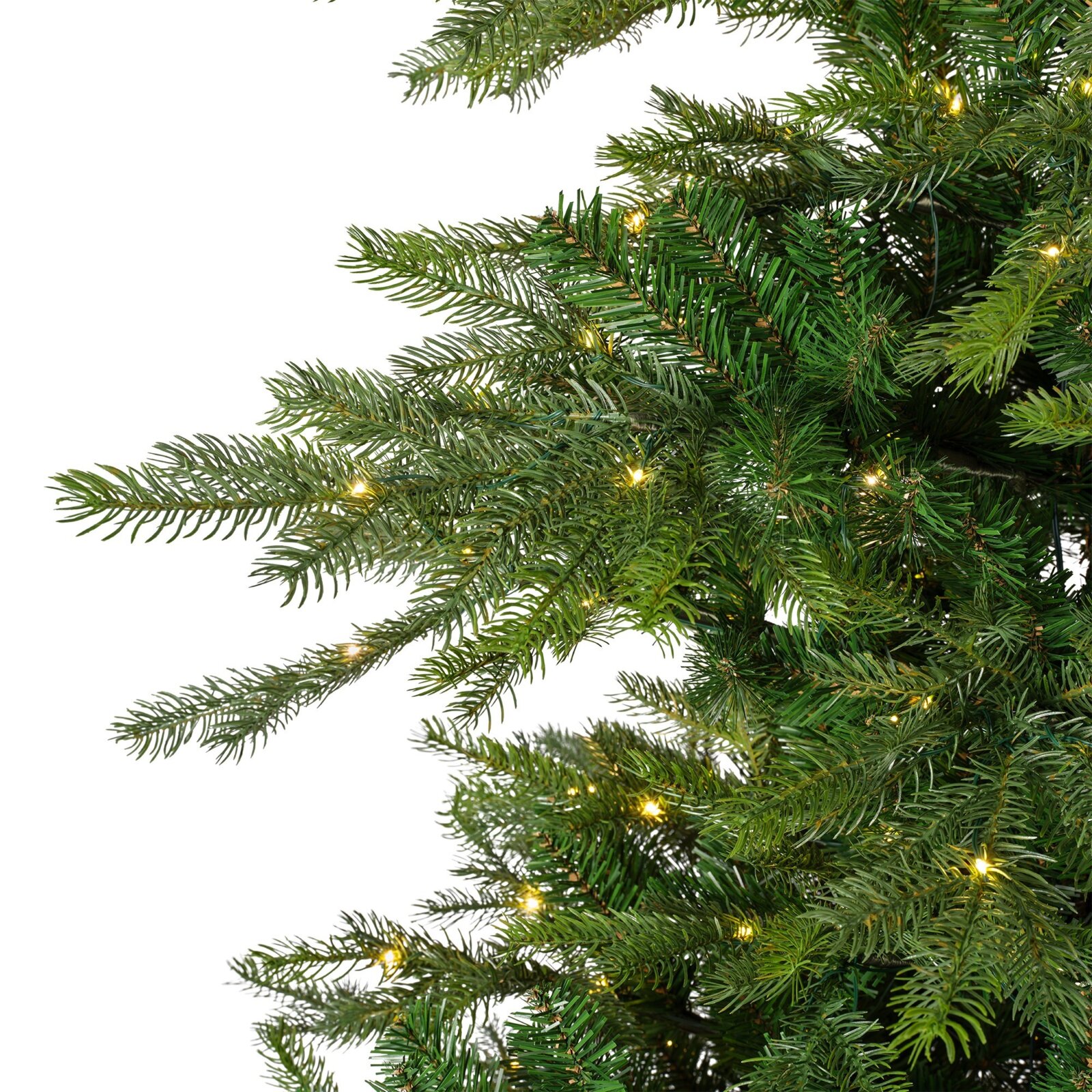 Close-up vanuit zijperspectief van een volle groene kunstkerstboom met warmwitte verlichting en natuurgetrouwe naaldtakken tegen een witte achtergrond.