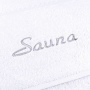 Nahaufnahme eines weißen Saunatuchs mit grauer Stickerei des Wortes 'Sauna'.
