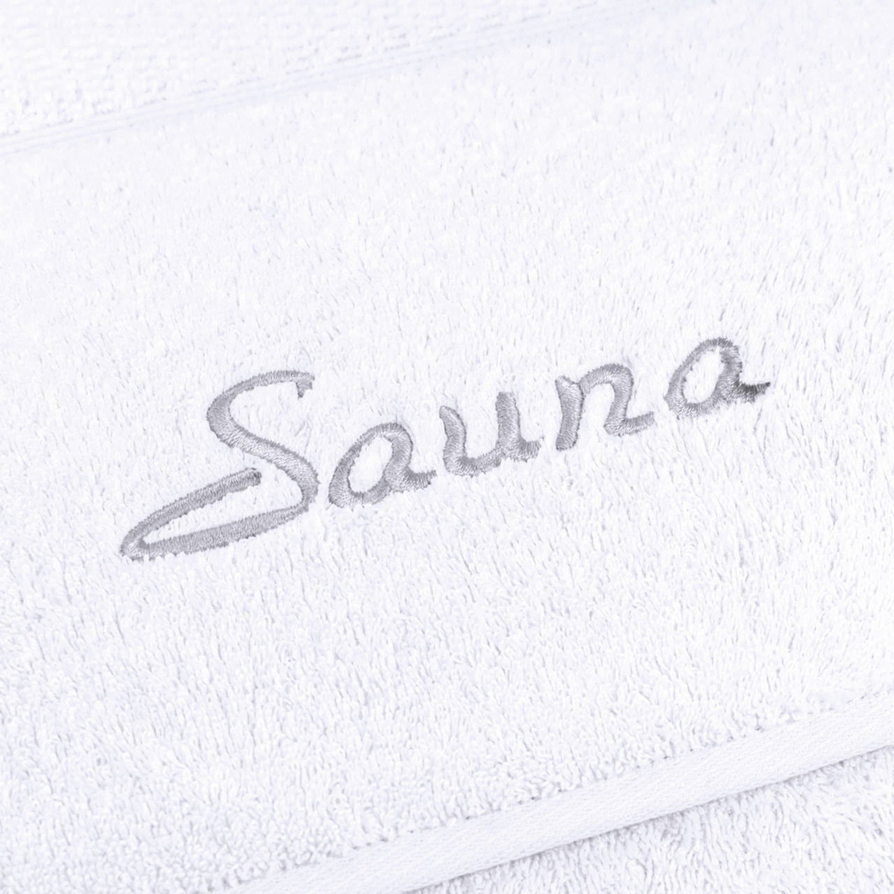 Nahaufnahme eines weißen Saunatuchs mit grauer Stickerei des Wortes 'Sauna'.
