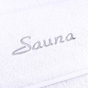 Nahaufnahme eines weißen Saunatuchs mit grauer Stickerei des Wortes 'Sauna'.